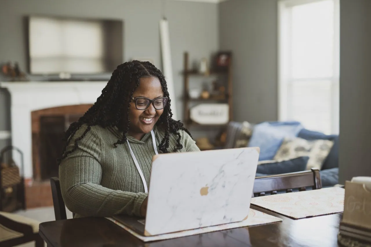 A woman smiling while using her laptop at home in her living room